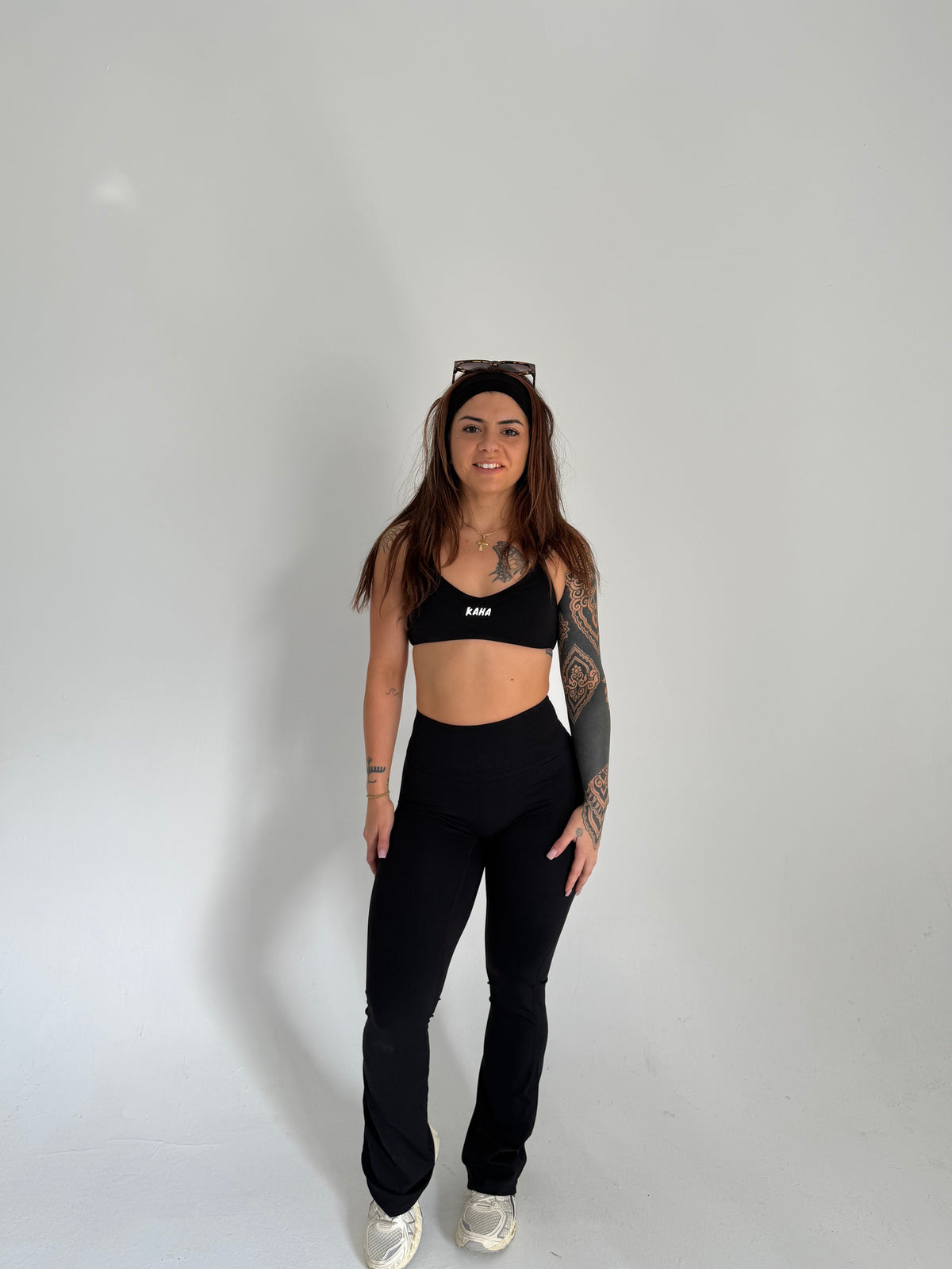 A woman wearing a black KAHA athletic sports bra and matching high-waisted flared leggings against a white background.