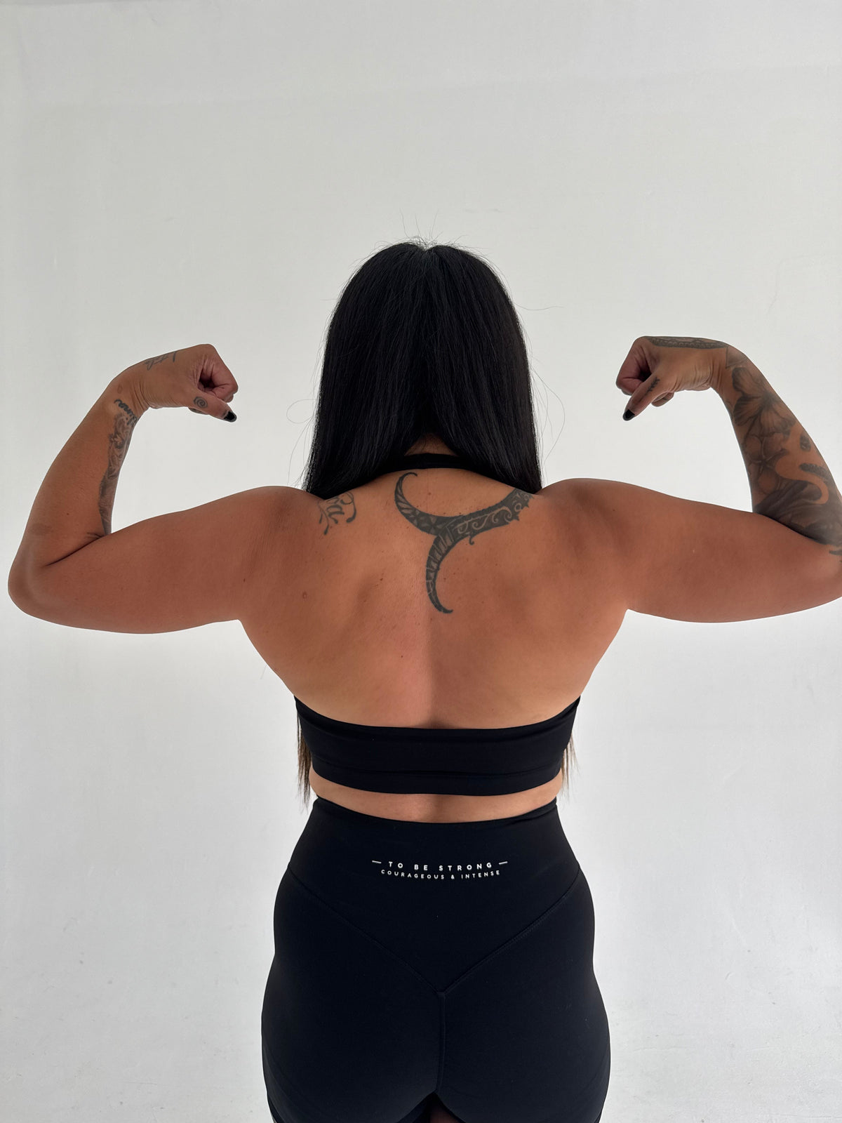KAHA black athletic sports bra and high-waisted shorts set worn by a woman flexing her back muscles