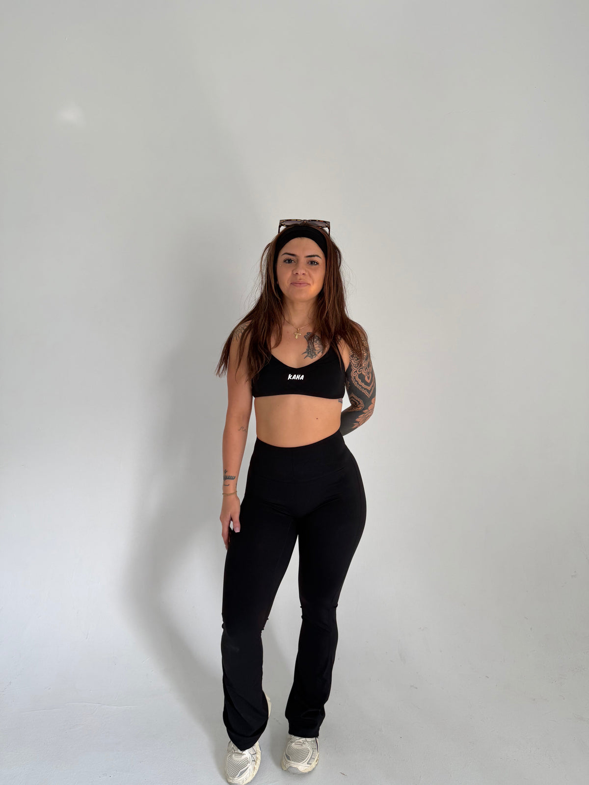 A woman wearing a black KAHA athletic sports bra and high-waisted flared leggings against a plain white background.