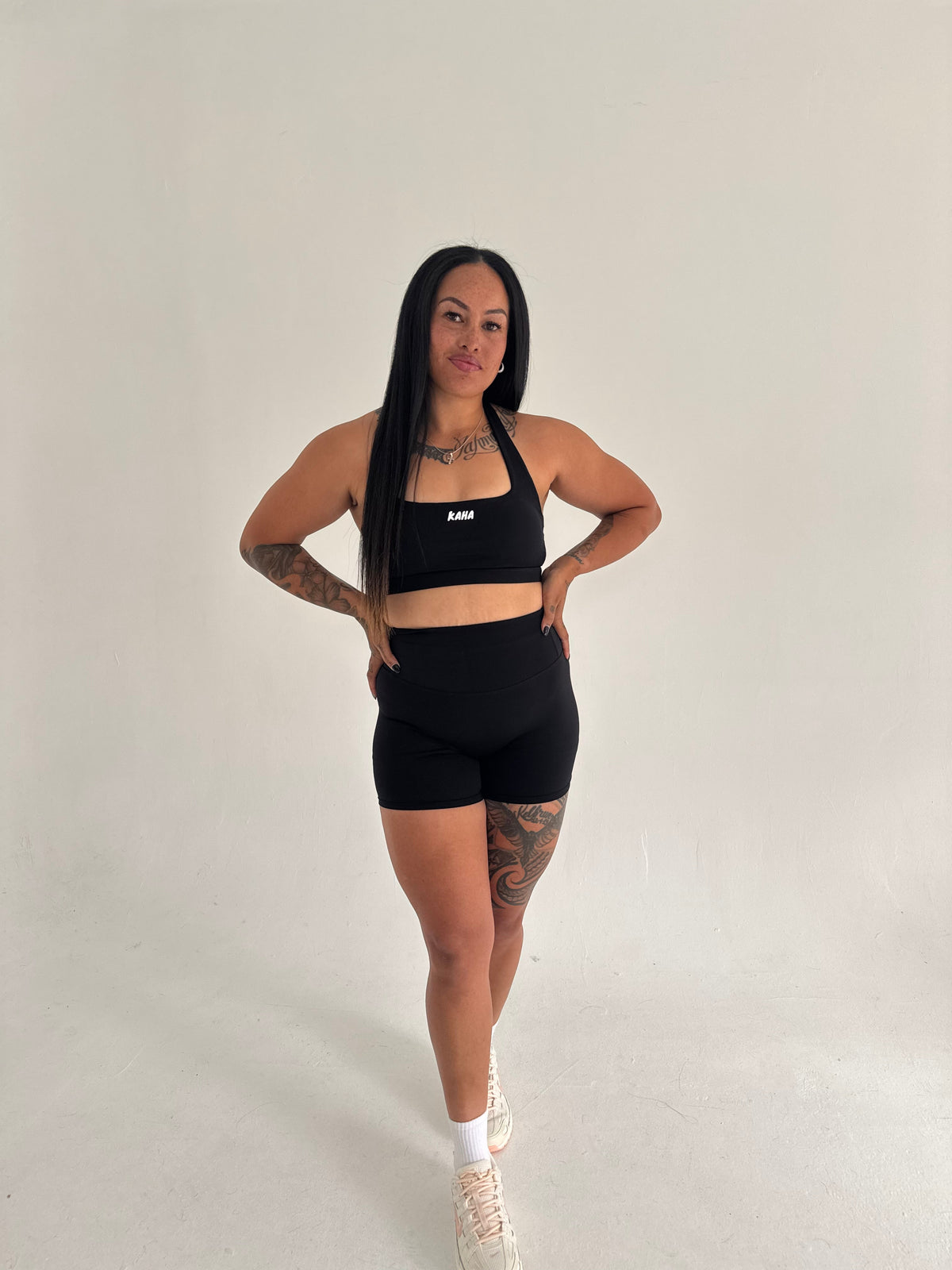 A model wearing KAHA black high-waisted scrunch shorts and a matching sports bra in a studio setting.