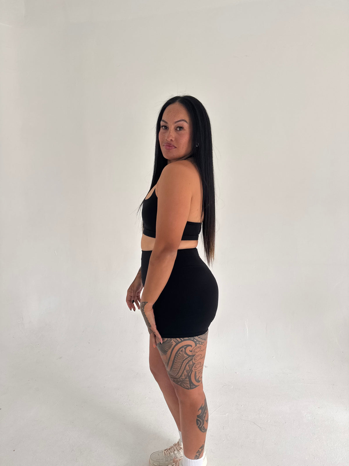 Model wearing KAHA high-waisted black scrunch shorts with V-shaped back contour, side profile view