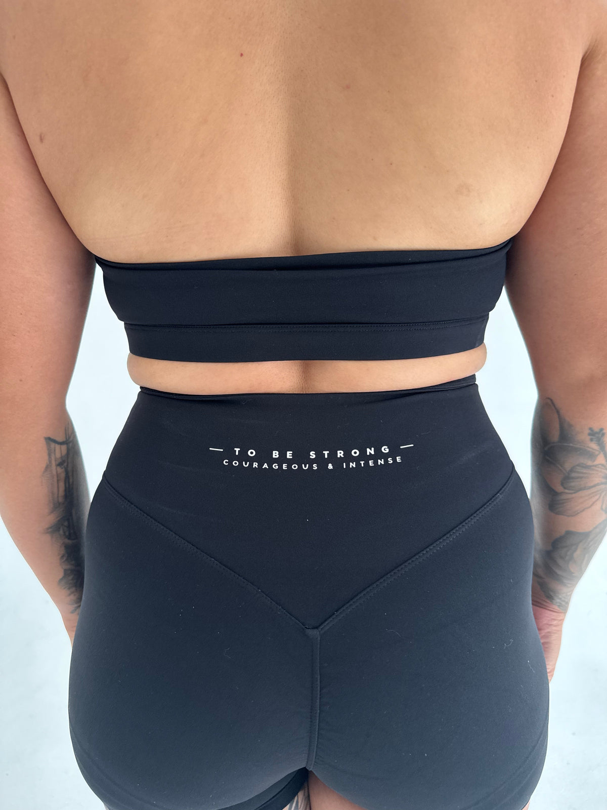 Back view of a person wearing a KAHA black athletic sports bra and matching shorts with motivational text print