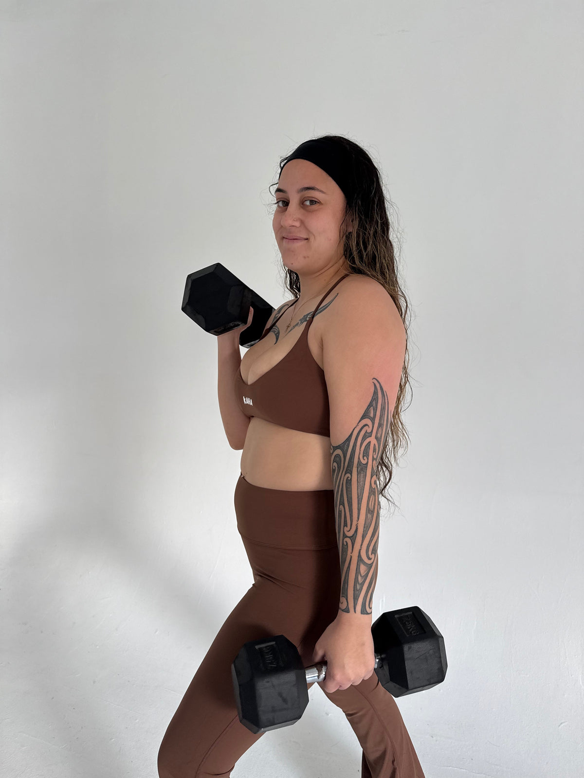 KAHA matching brown sports bra and flare leggings set worn by a woman holding dumbbells in a studio setting