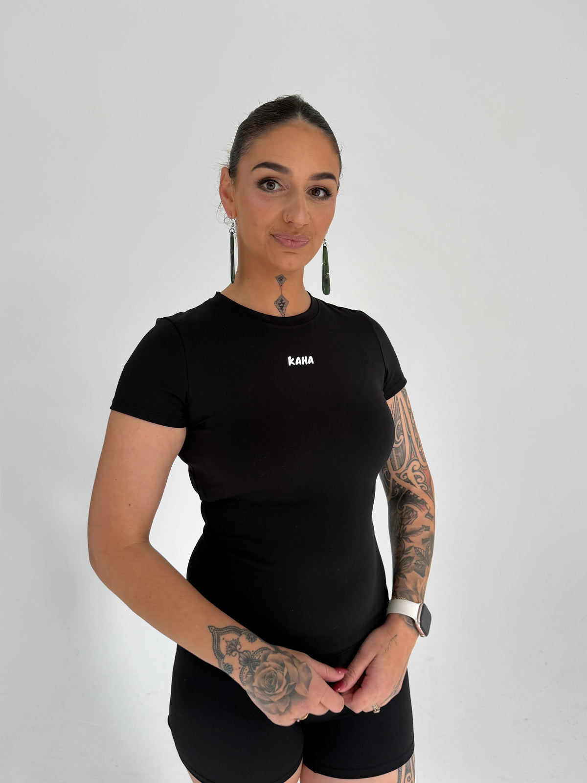 A woman wearing a KAHA fitted black short sleeve performance t-shirt with a crew neckline against a white background.
